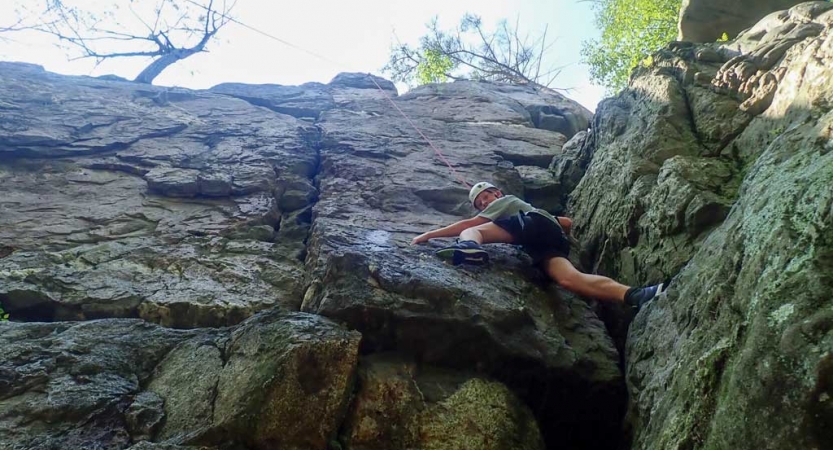 a teen scales a rock wall on a rock climbing trip with outward bound